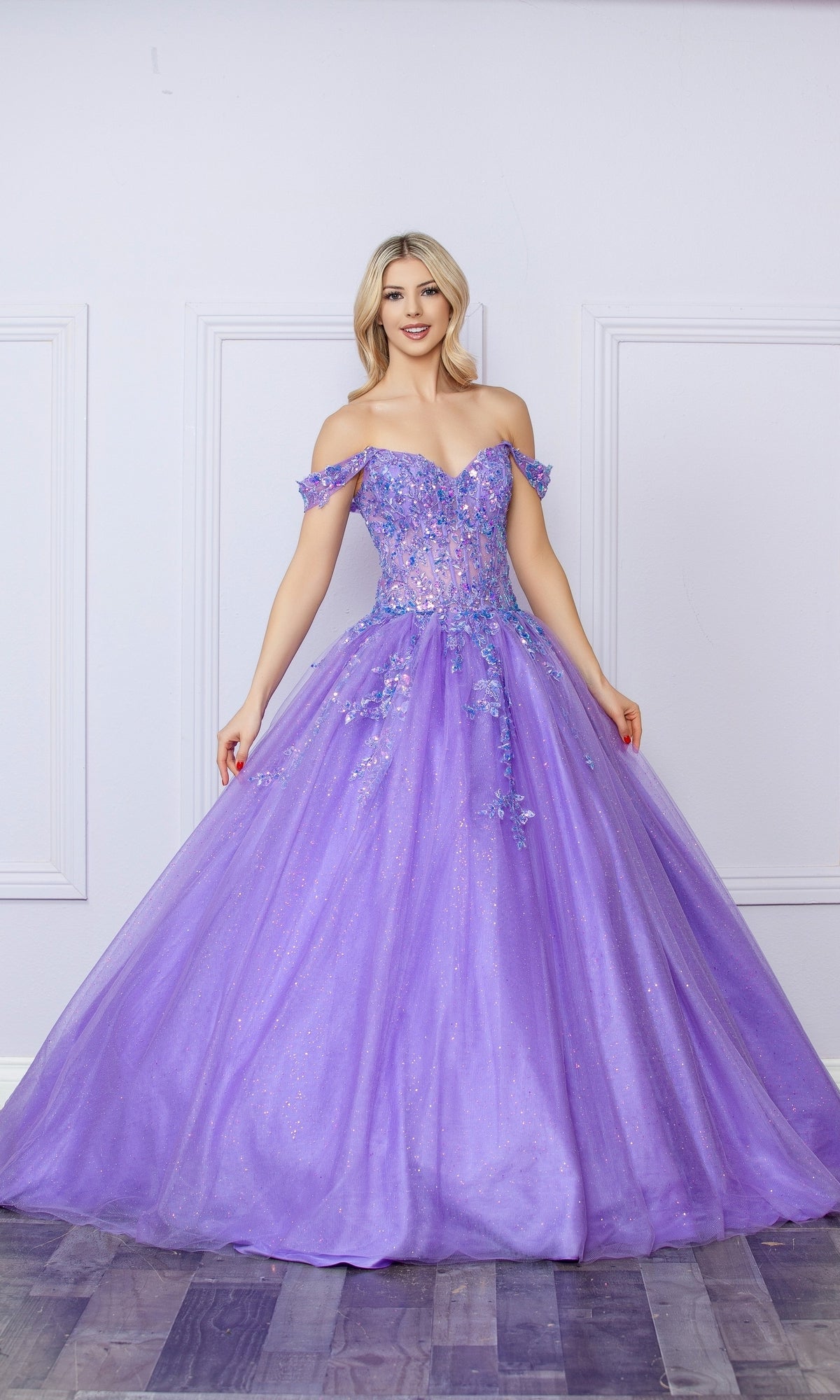 Woman in the Bright Off-the-Shoulder Long Prom Ball Gown H1349, featuring a lavender hue, floral accents, and a full tulle skirt, stands against a white wall with panel molding.
